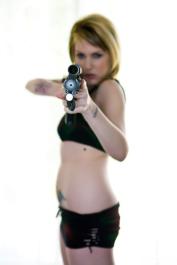Sassy gun toting cutie Envy strips on the bed to spread her chubby ass